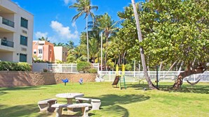 A courtyard with a picnic table, palm trees, and a playground. - Crystal Blue (Luquillo)