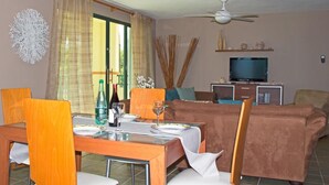 A dining area with a table set for two, a sofa, and a television in the background. - Crystal Blue (Luquillo)