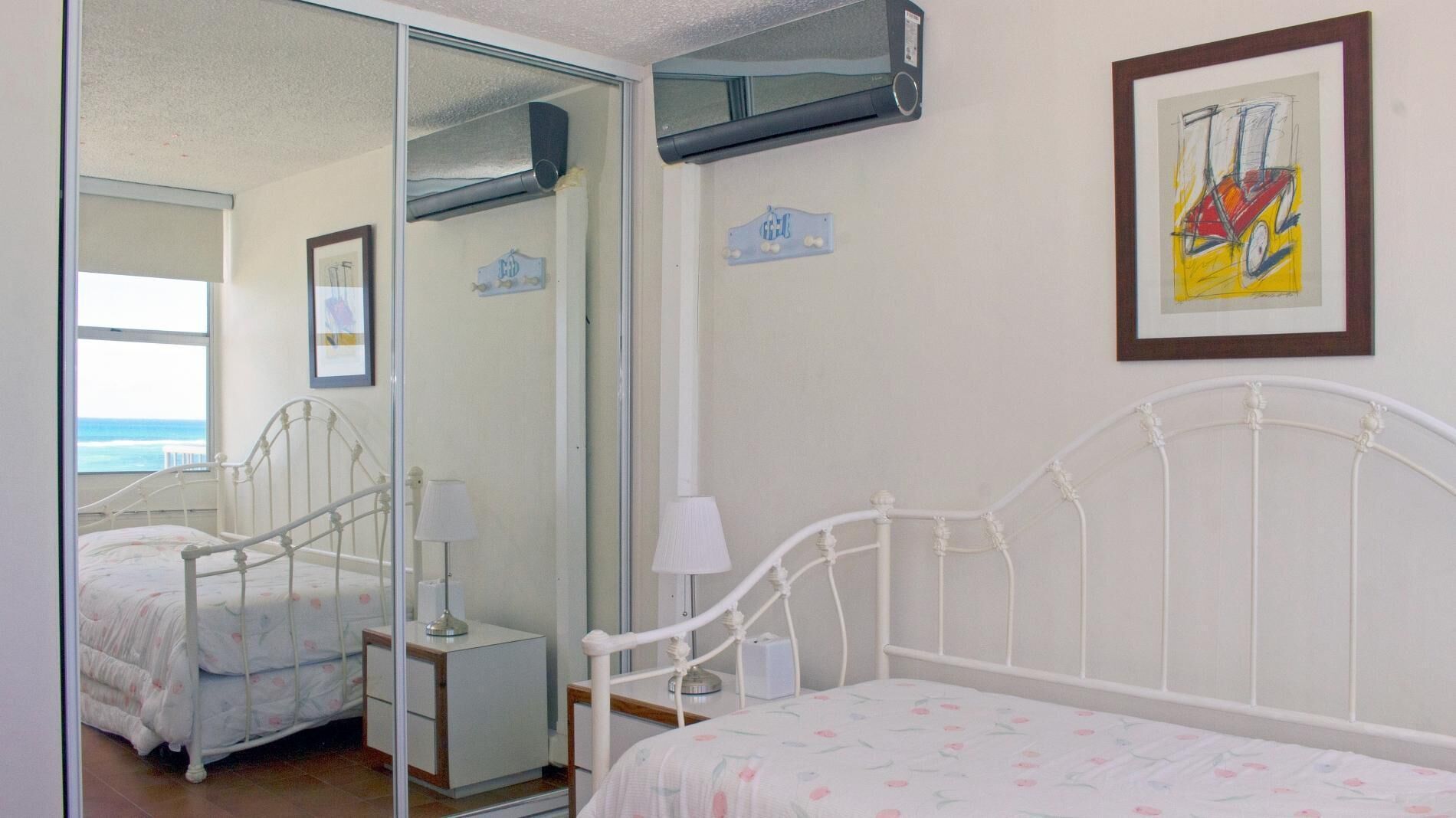 Quarto com cama, mesa de cabeceira, abajur, espelho e um quadro na parede.