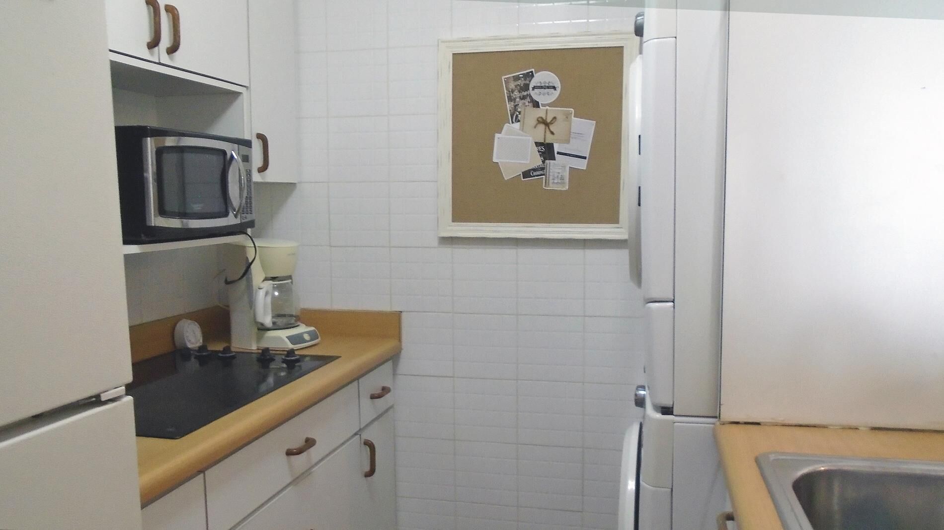 A compact kitchen with white cabinets, a microwave, a coffee maker, and a refrigerator.
