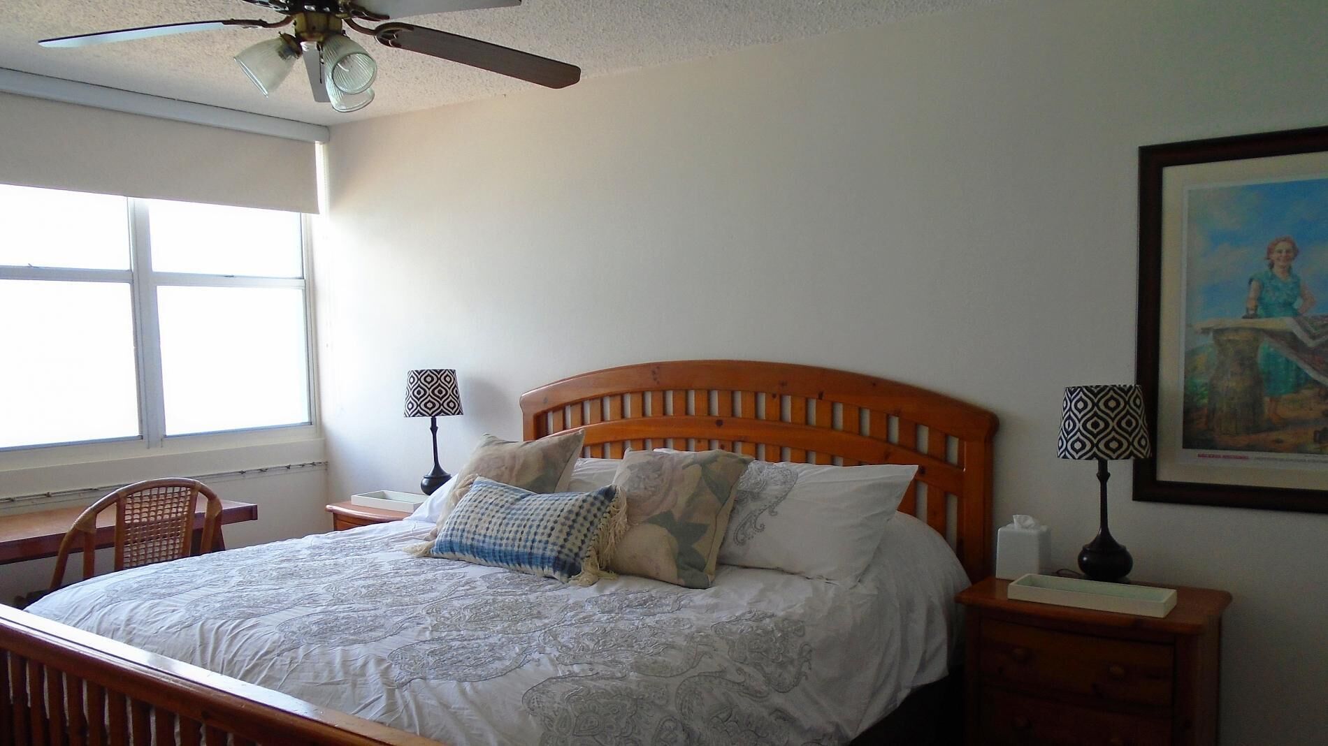 A bedroom with a wooden bed, two bedside tables, a ceiling fan, a window, and a framed picture on the wall.