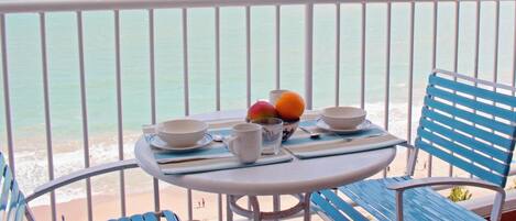 A balcony with a table set for two, overlooking a beach.