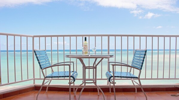 A balcony with two chairs and a table, overlooking a beach with clear turquoise water.