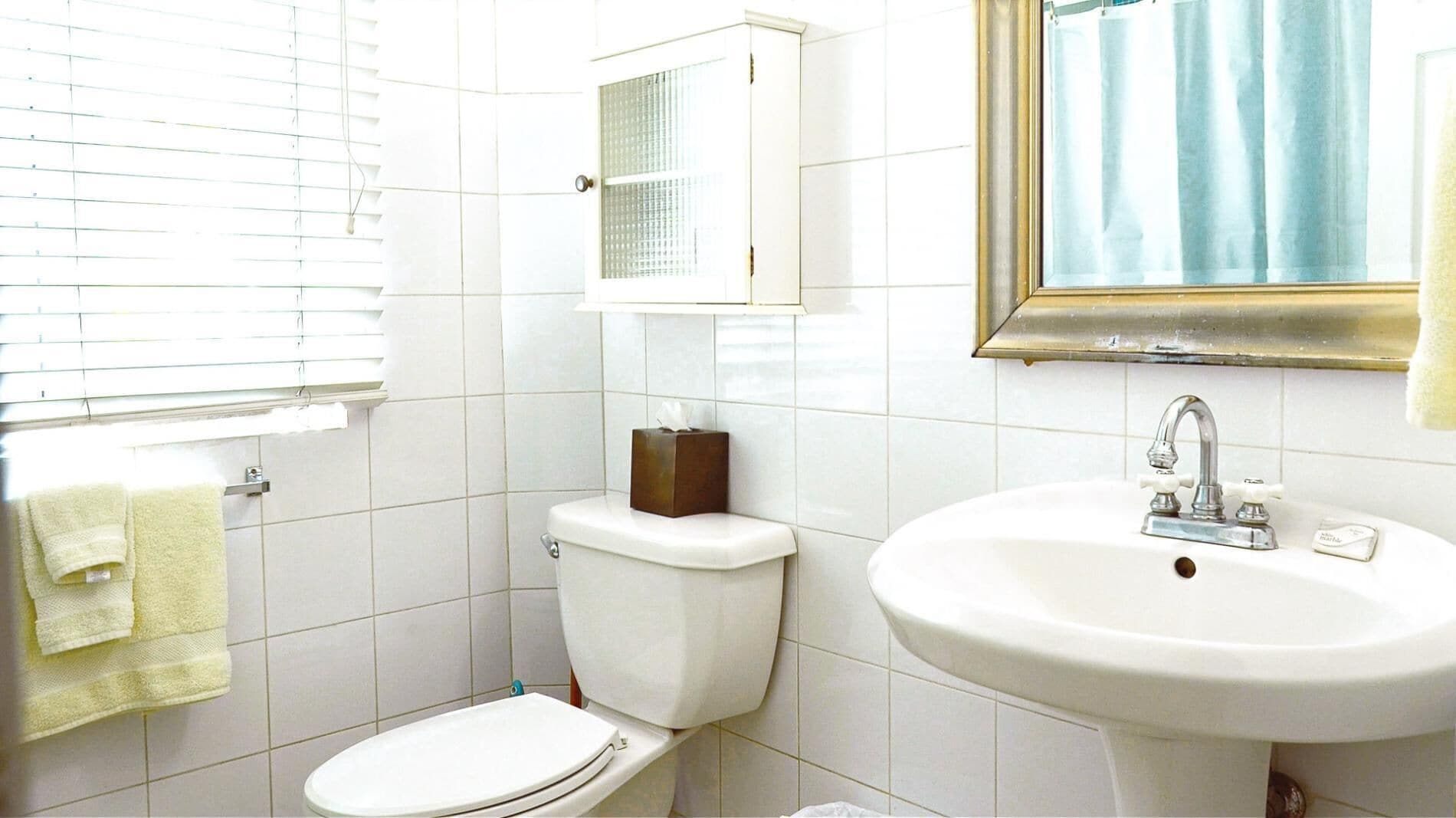 A bathroom with a toilet, sink, and window with blinds.