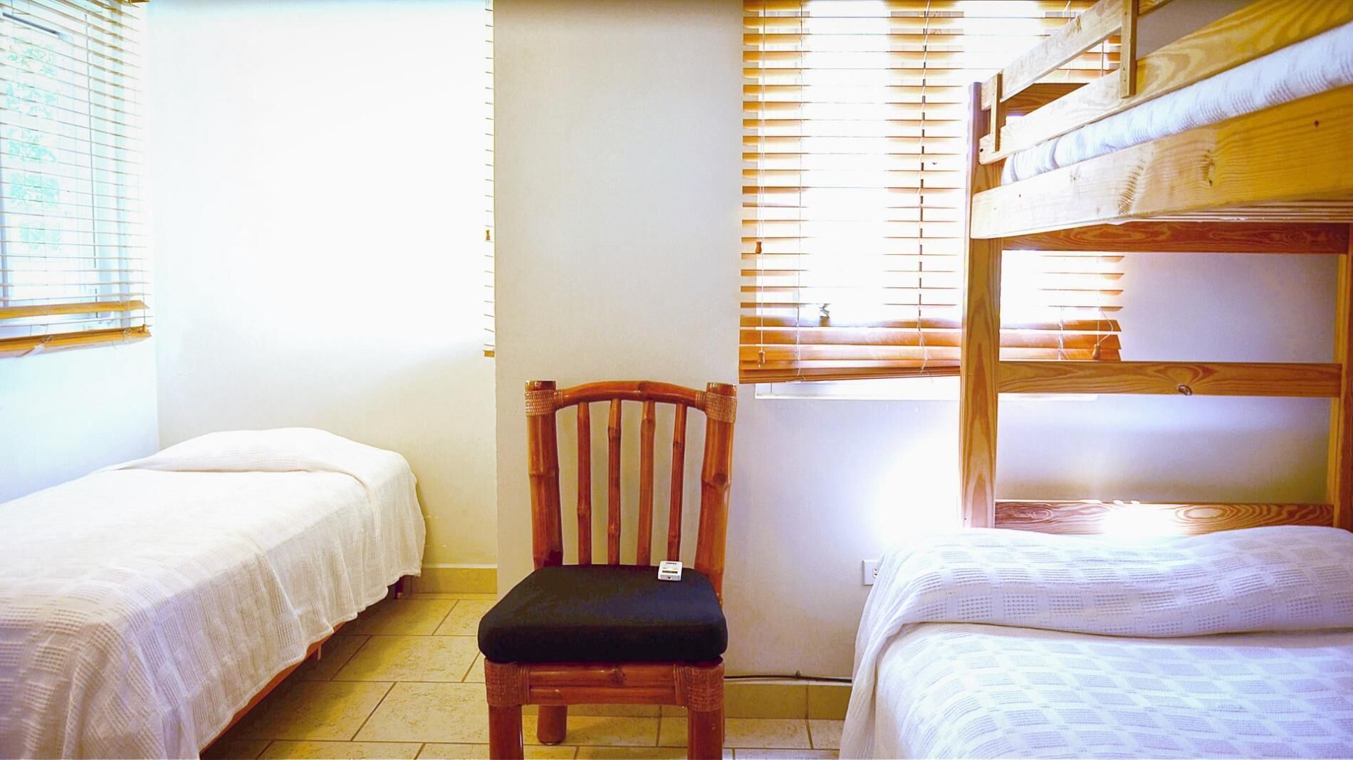 A dormitory room with two single beds, a wooden chair, and a bunk bed.