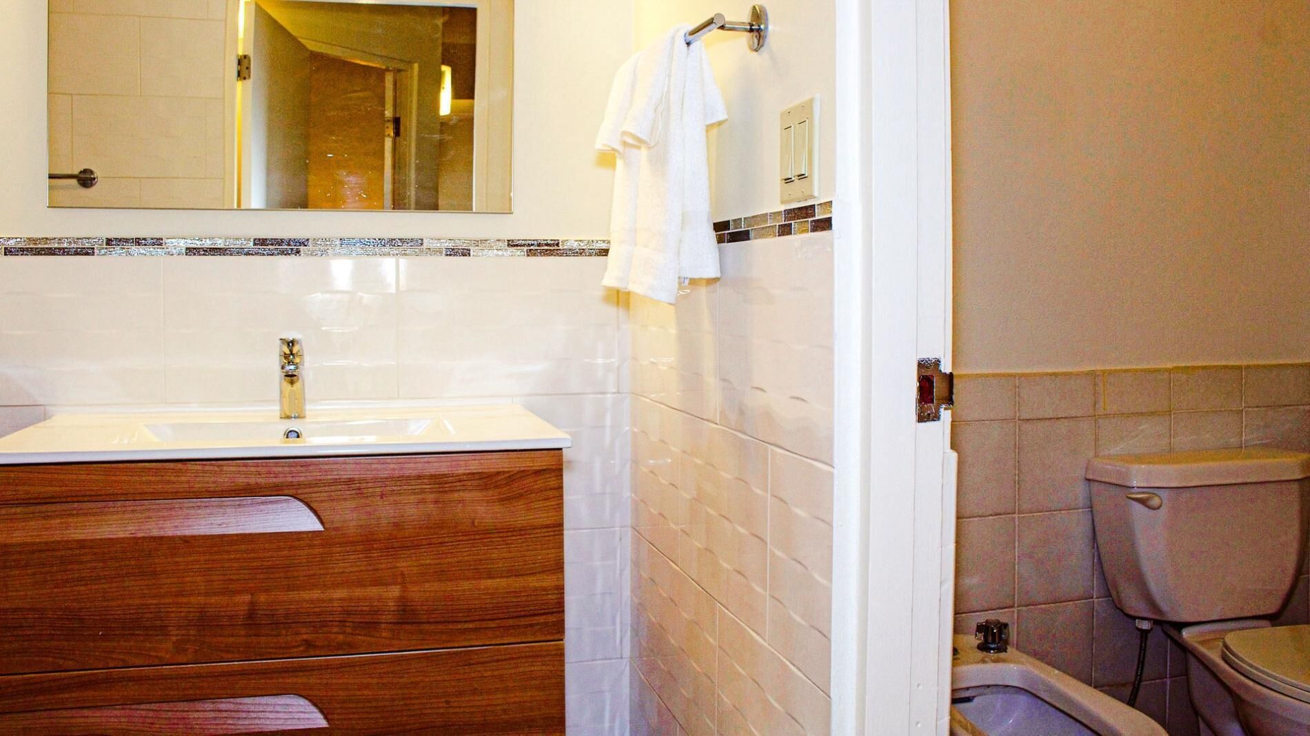 A bathroom with a wooden vanity, a mirror, a toilet, and a shower area.