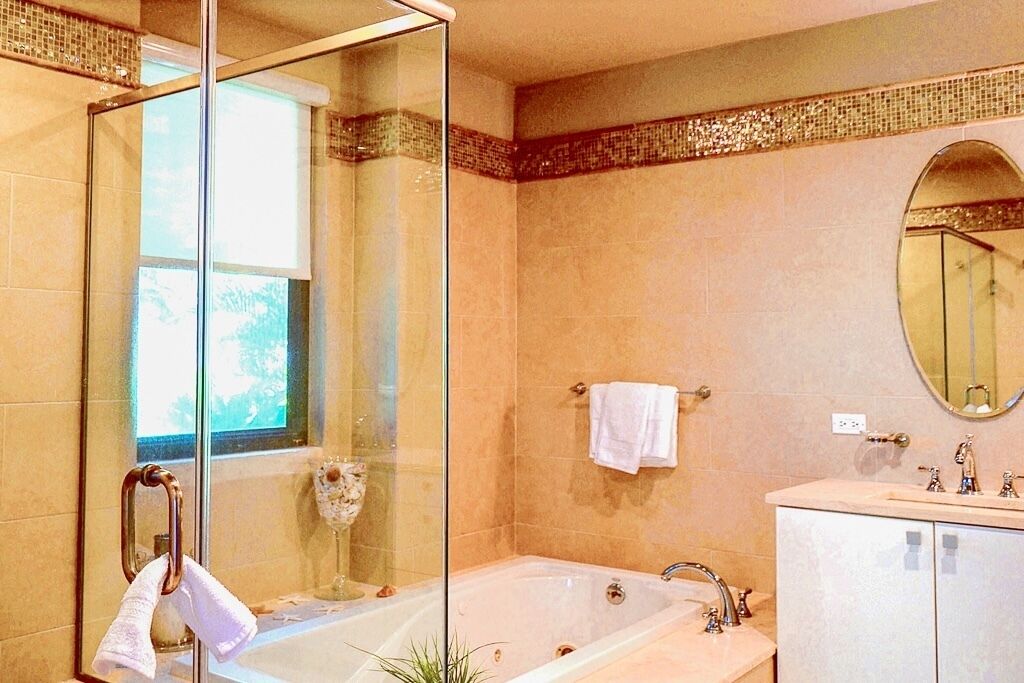 A bathroom with a glass-enclosed shower, a bathtub, a sink with a vanity, and a mirror.