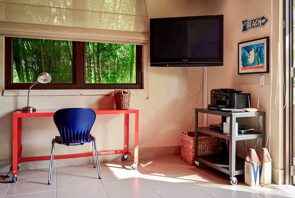 A room with a desk, chair, TV, and shelves.