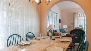 A dining area with a table set for four, chairs, and a view through an archway to a living room with a sofa and a lamp. - Villa Verde (San Juan)