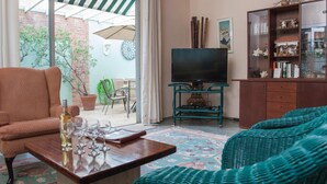 A living room with a sofa, a coffee table with glasses and a bottle, a TV on a stand, and a bookshelf. - Villa Verde (San Juan)