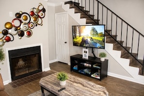 Een woonkamer met een open haard, een televisie op een dressoir, een trap en een wand met decoratieve borden.