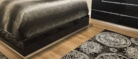 Un dormitorio con cama, cómoda, televisor y alfombras estampadas.