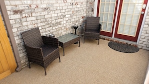 Een terras met rieten meubels, een glazen tafel en een bakstenen muur.