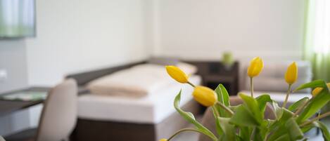 A modern hotel room with a bed, a desk, and a vase with yellow flowers.