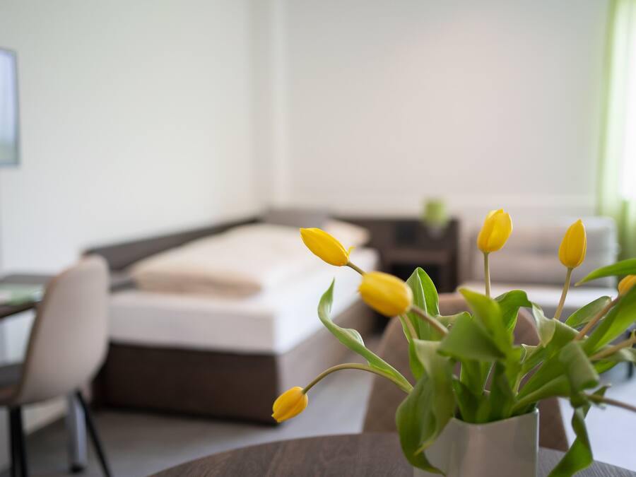 Ein modernes Hotelzimmer mit Bett, Schreibtisch und einer Vase mit gelben Blumen.