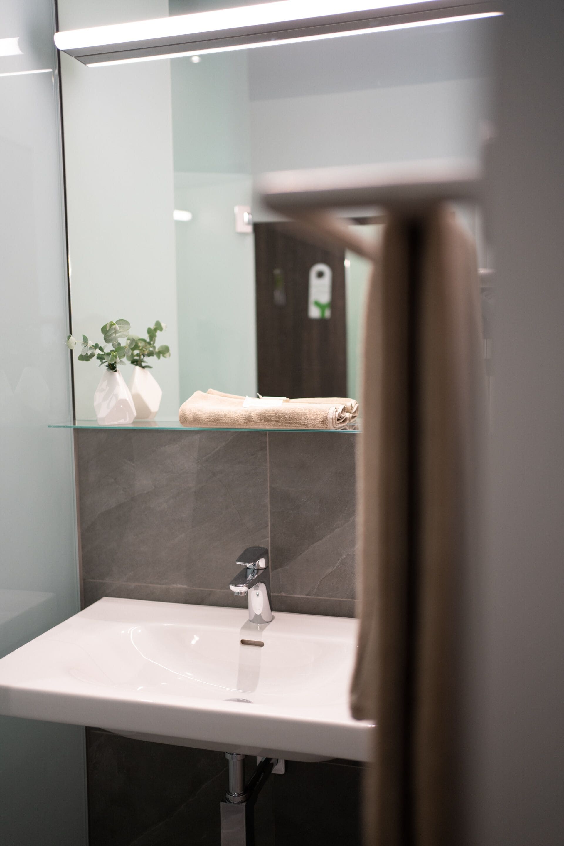 A modern bathroom with a glass shelf holding a towel and a vase with flowers.