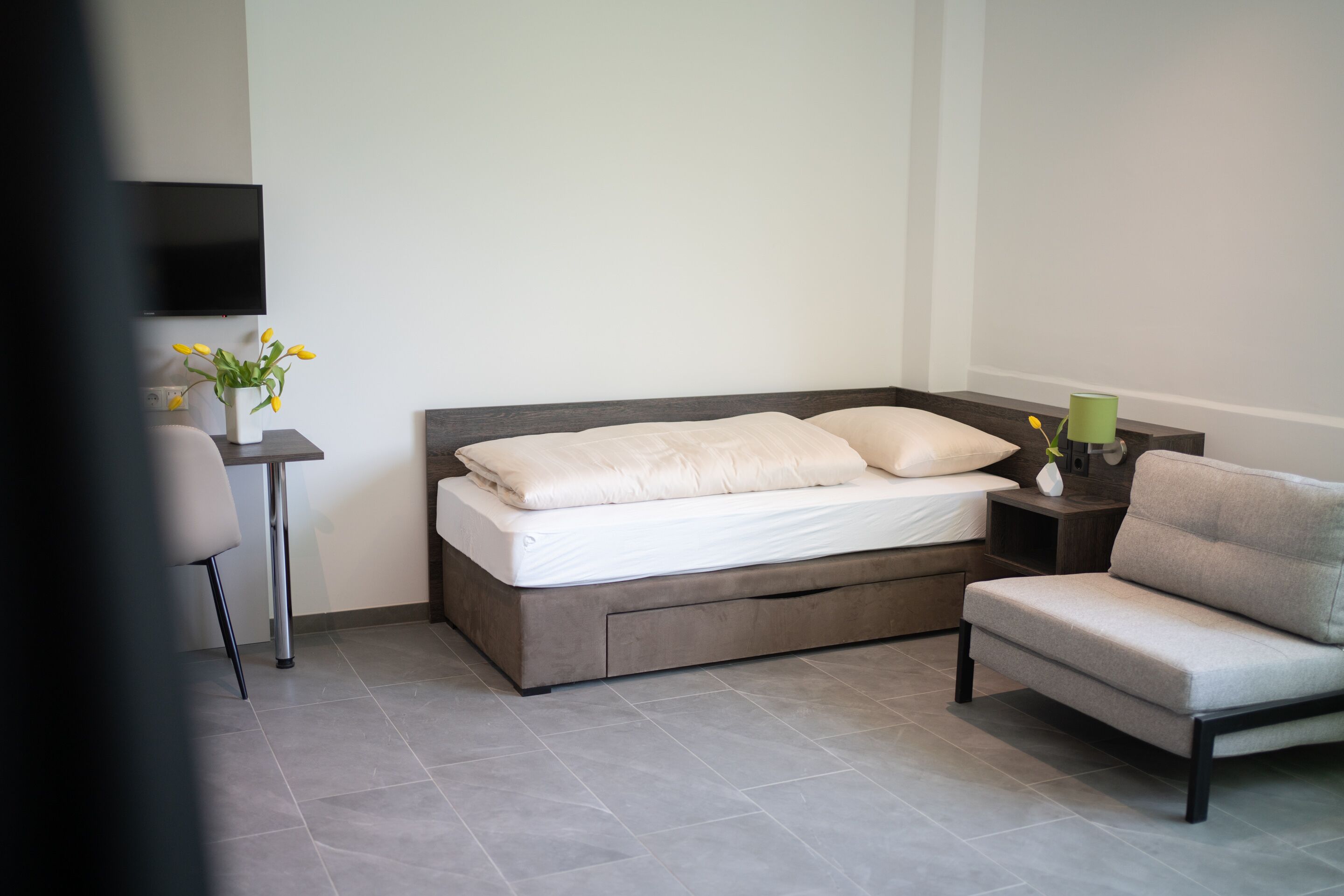 Une chambre moderne avec un lit, une chaise, une table de chevet et un téléviseur.