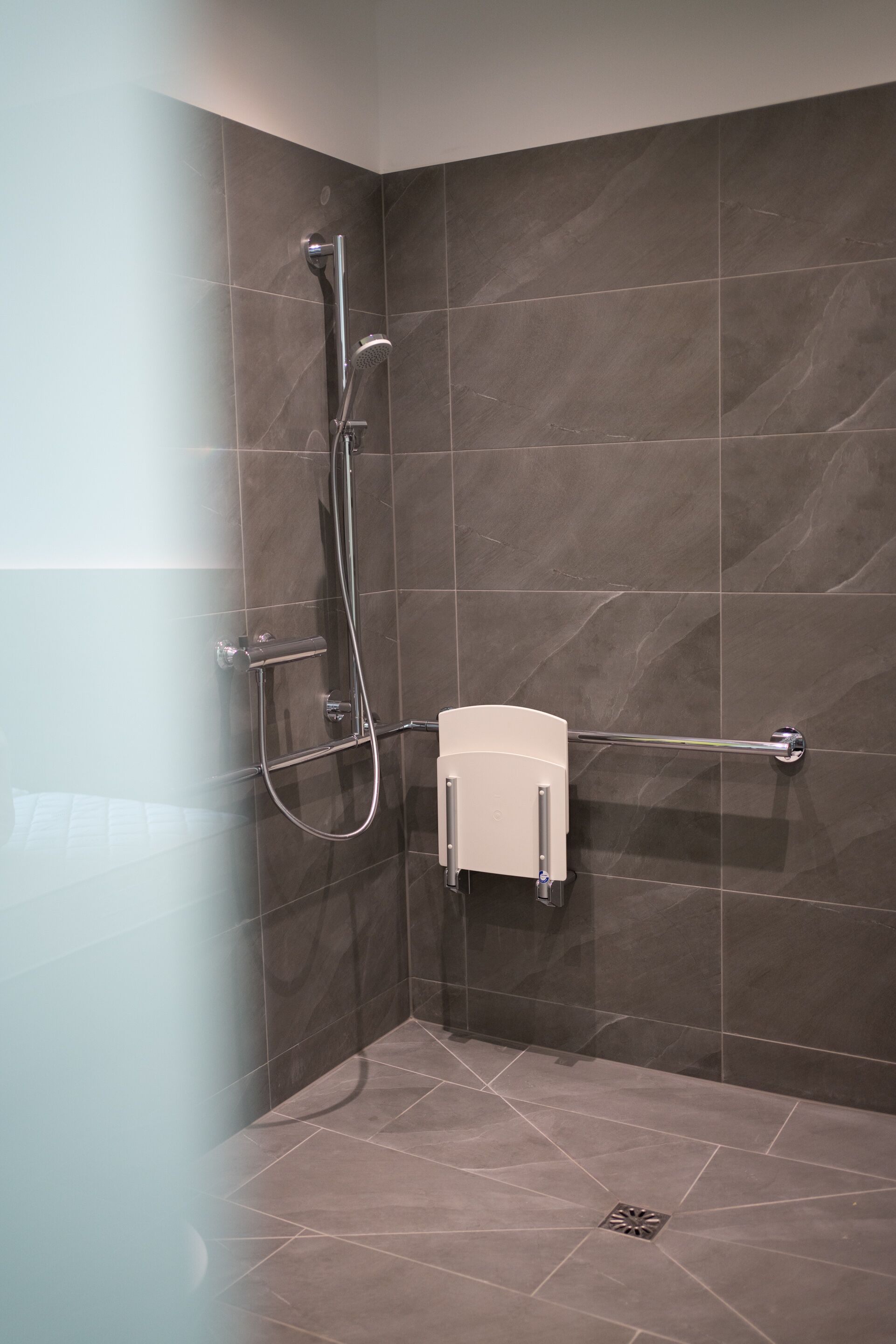 Zona de ducha con cabezal de ducha manual, toallero de pared y dispensador de jabón.