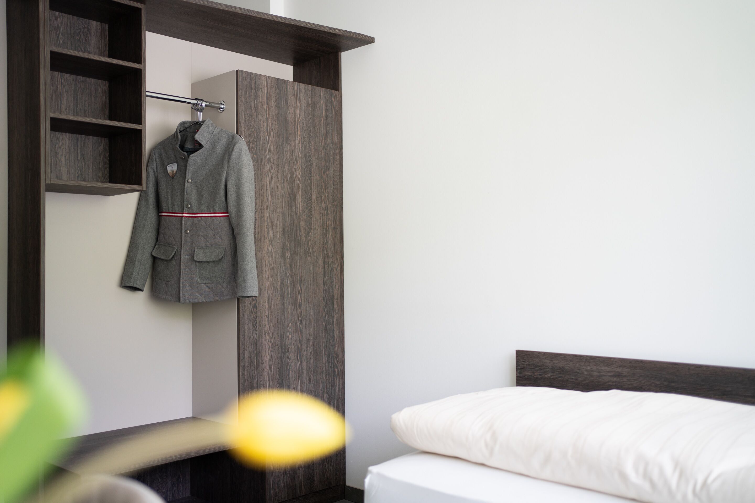 A modern bedroom with a bed, a wooden wardrobe, and a coat hanging on a rack.