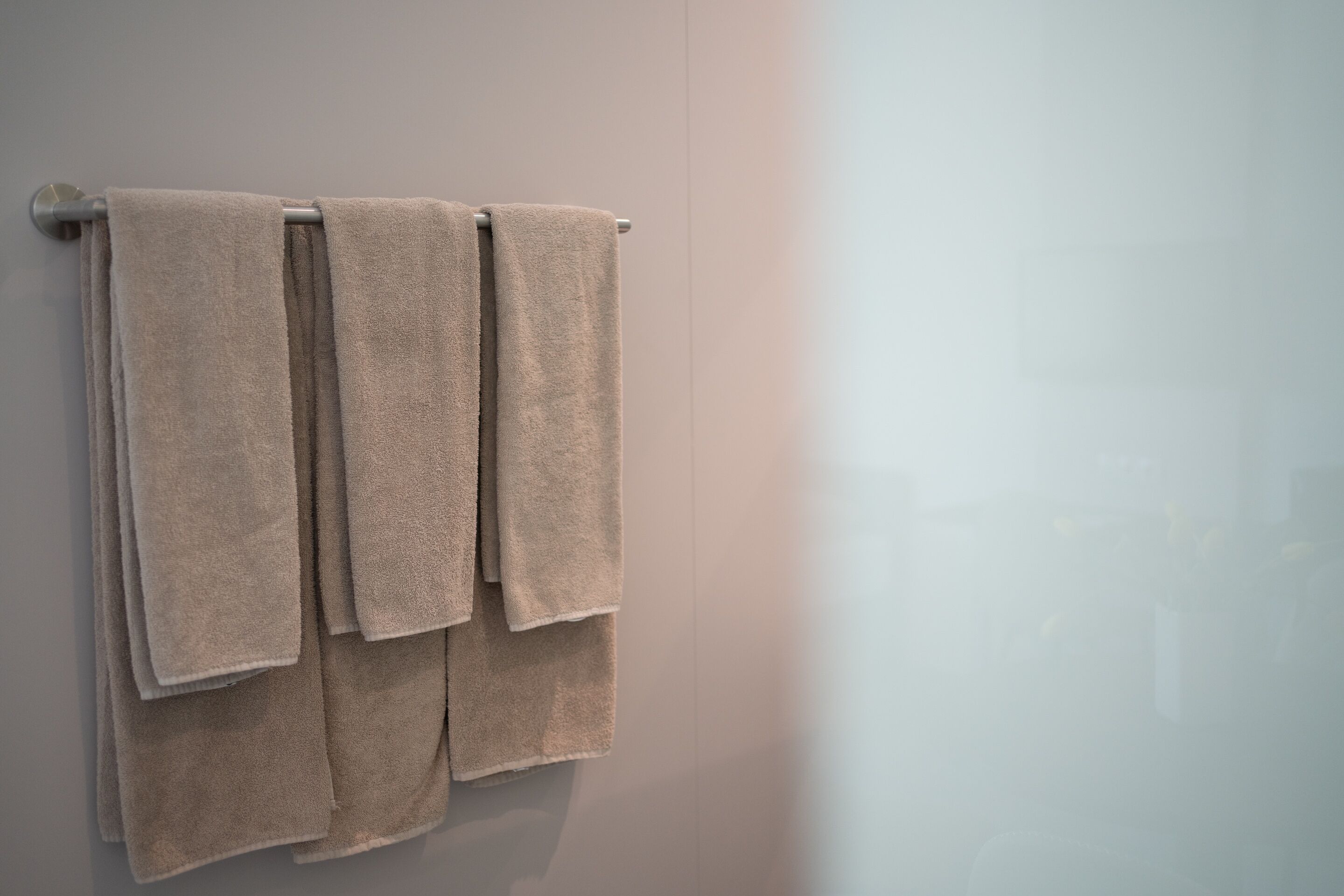 A bathroom with three beige towels hanging on a metal towel rack.