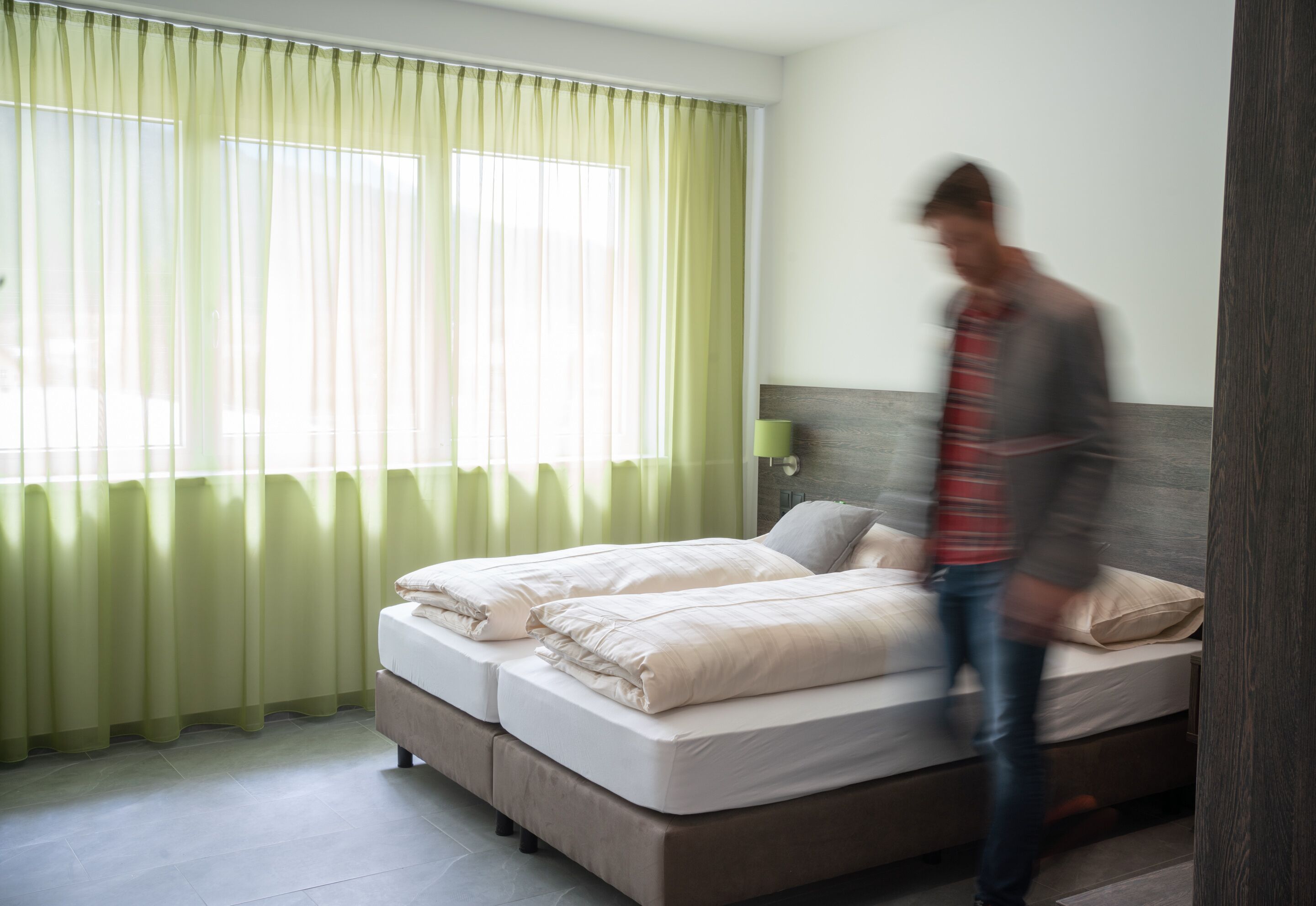 A hotel room with a bed, a nightstand, and a window with curtains.