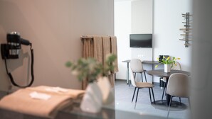 A modern hotel room with a glass partition, a flat-screen TV mounted on the wall, a dining area with a round table and chairs, and a plant in a vase. - eee hotel Liezen (Liezen)