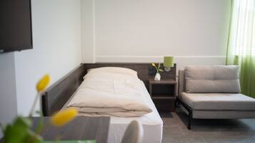 Una habitación de hotel con cama, mesita de noche, una silla, televisión y ventana con cortinas.