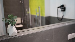 A bathroom with a white vase on a counter, a mirror reflecting a shower area, and a green accent wall. - eee hotel Liezen (Liezen)