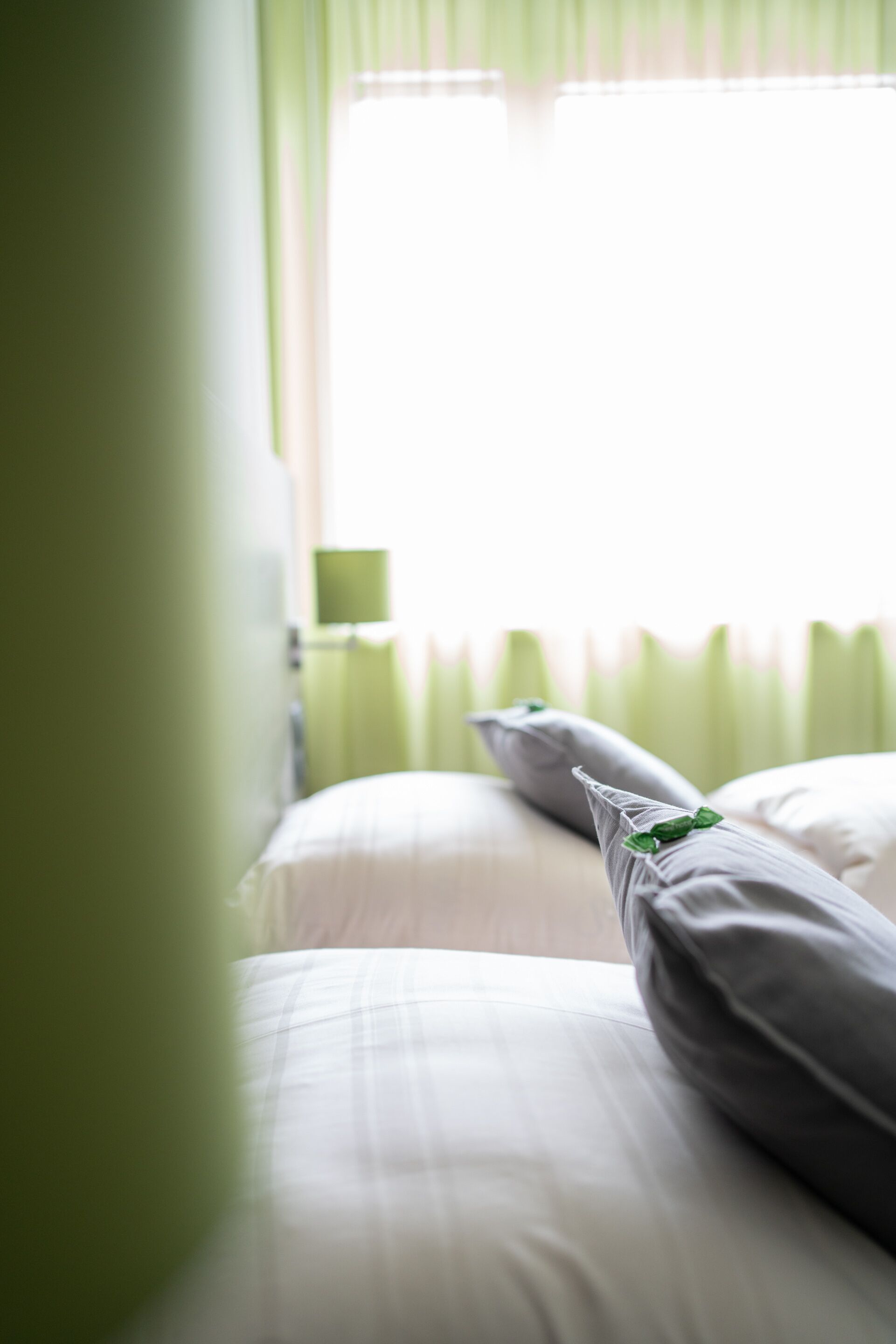 A bed with white linens and a pillow with a green leaf decoration.