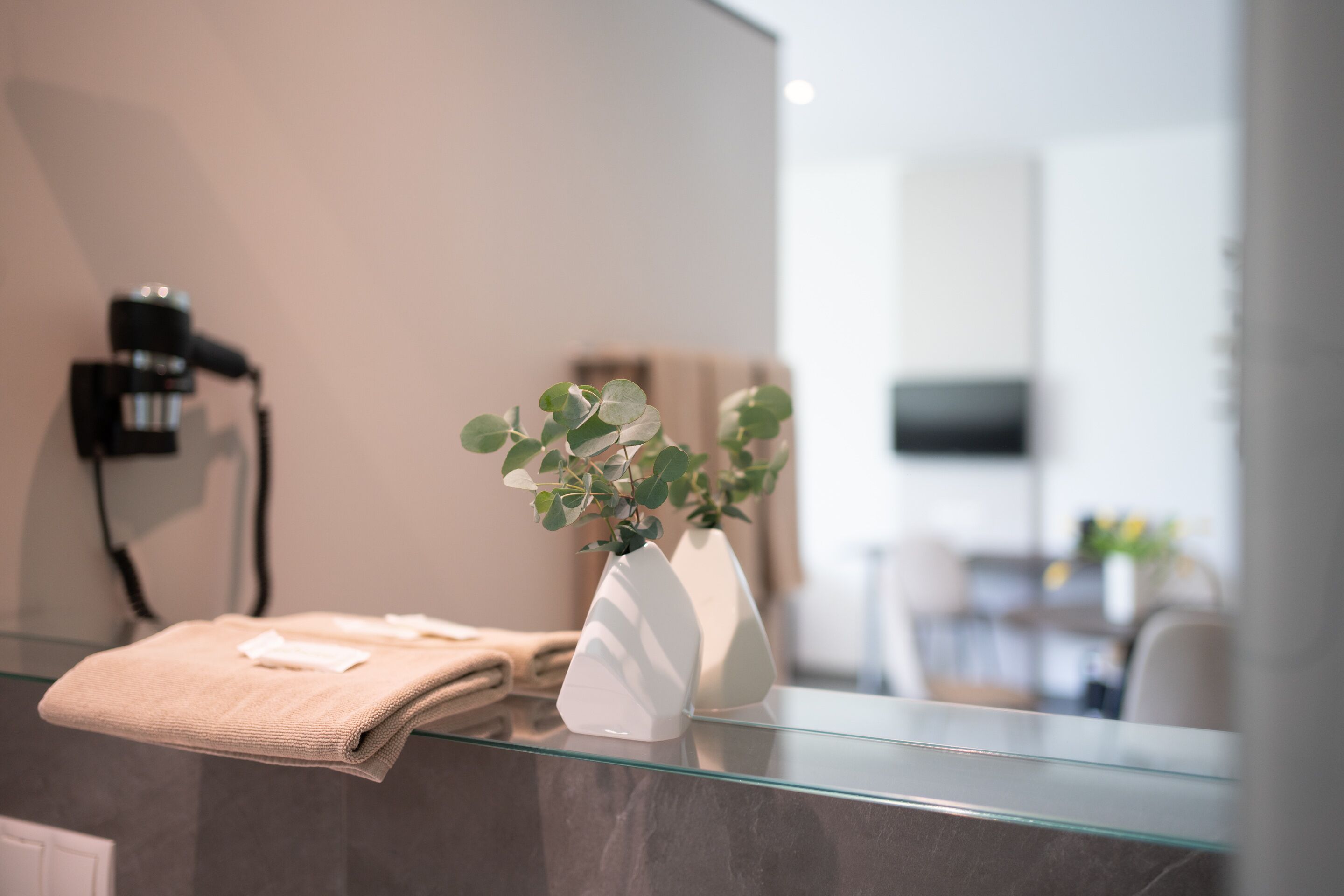 Een badkamer met een glazen aanrecht, een handdoek en een witte vaas met een plant.