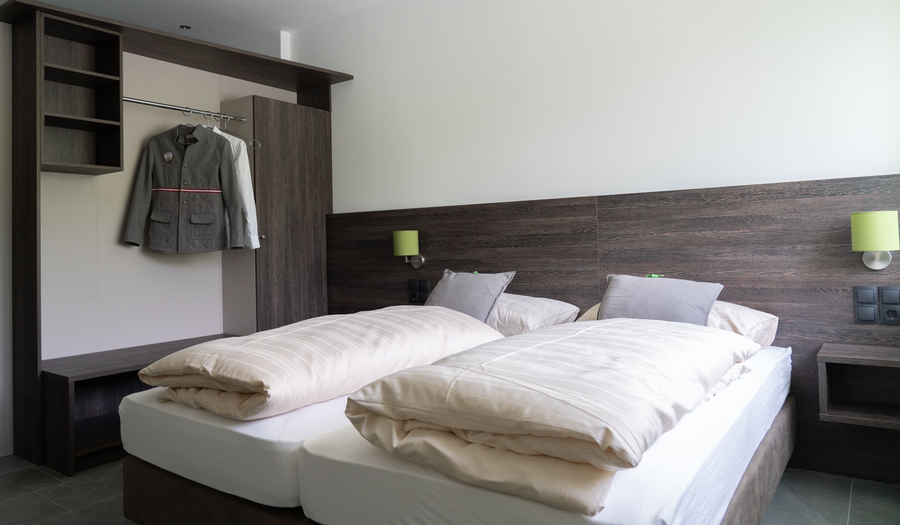 Una habitación de hotel moderna con una cama doble, una mesita de noche, un armario y una lámpara de pared.