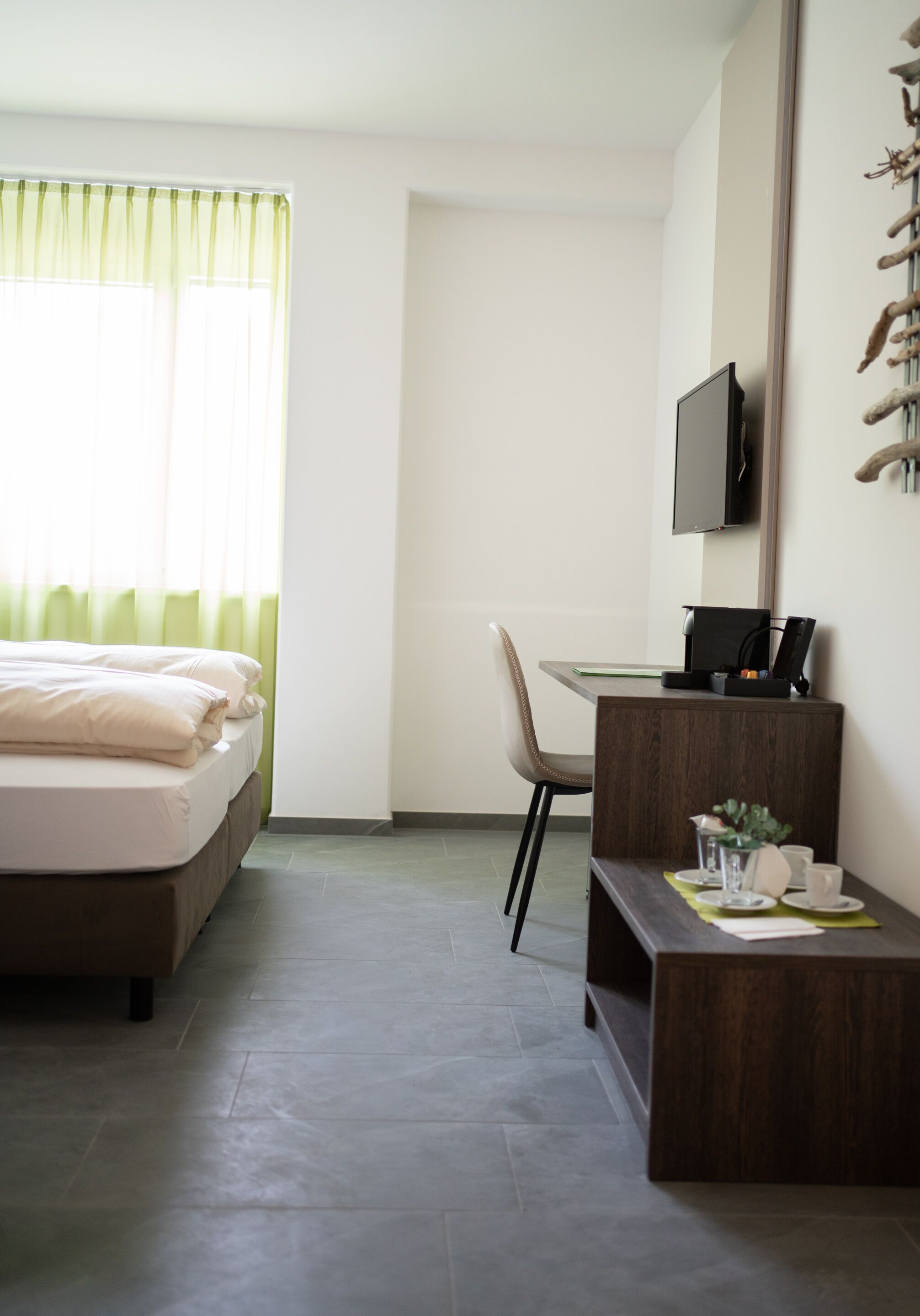 Una habitación de hotel con una cama, un escritorio, una silla, un televisor y una mesita con una taza y una planta.