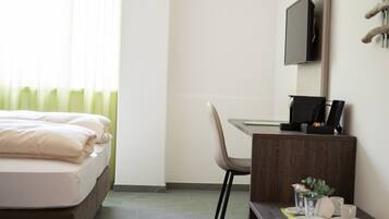 Ein Hotelzimmer mit Bett, Schreibtisch, Stuhl, Fernseher und einem kleinen Tisch mit Tasse und Pflanze.