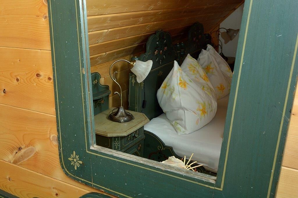 Ein Holzhütten-Zimmer mit einem Bett, einem kleinen Tisch mit Lampe und einem Spiegel, der das Zimmerinnere widerspiegelt.