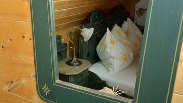 Ein Holzhütten-Zimmer mit einem Bett, einem kleinen Tisch mit Lampe und einem Spiegel, der das Zimmerinnere widerspiegelt.