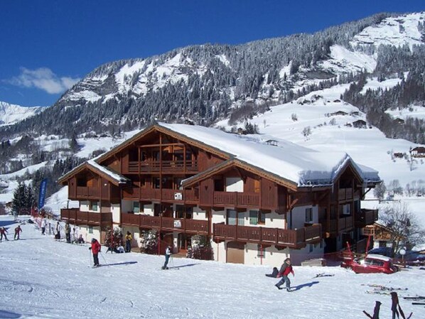 A wooden chalet with a balcony, surrounded by snow-covered mountains.