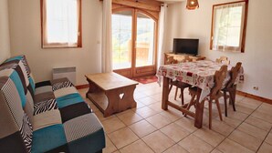A cozy living room with a sofa, a wooden coffee table, a dining table with chairs, a television, and large windows with curtains. - Ski-in/ski-out apartment with terrace, pet-friendly, Flumet (Flumet)