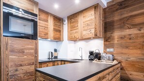 A kitchen with wooden cabinetry, a built-in oven, a coffee maker, and a sink. - Renovated Apartment · Near Center · Ski-In/Ski-Out · South-Facing Balcony (Val-d'Isère)