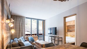 A modern room with a wooden dining table, a sofa, a TV, and large windows. - Renovated Apartment · Near Center · Ski-In/Ski-Out · South-Facing Balcony (Val-d'Isère)