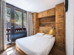 Une chambre avec un grand lit, des murs lambrissés, une fenêtre avec des rideaux et une vue sur les arbres.