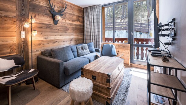 A cozy living room with a wooden wall, a sofa, a coffee table, and a television. - Renovated Apartment · Near Center · Ski-In/Ski-Out · South-Facing Balcony (Val-d'Isère)