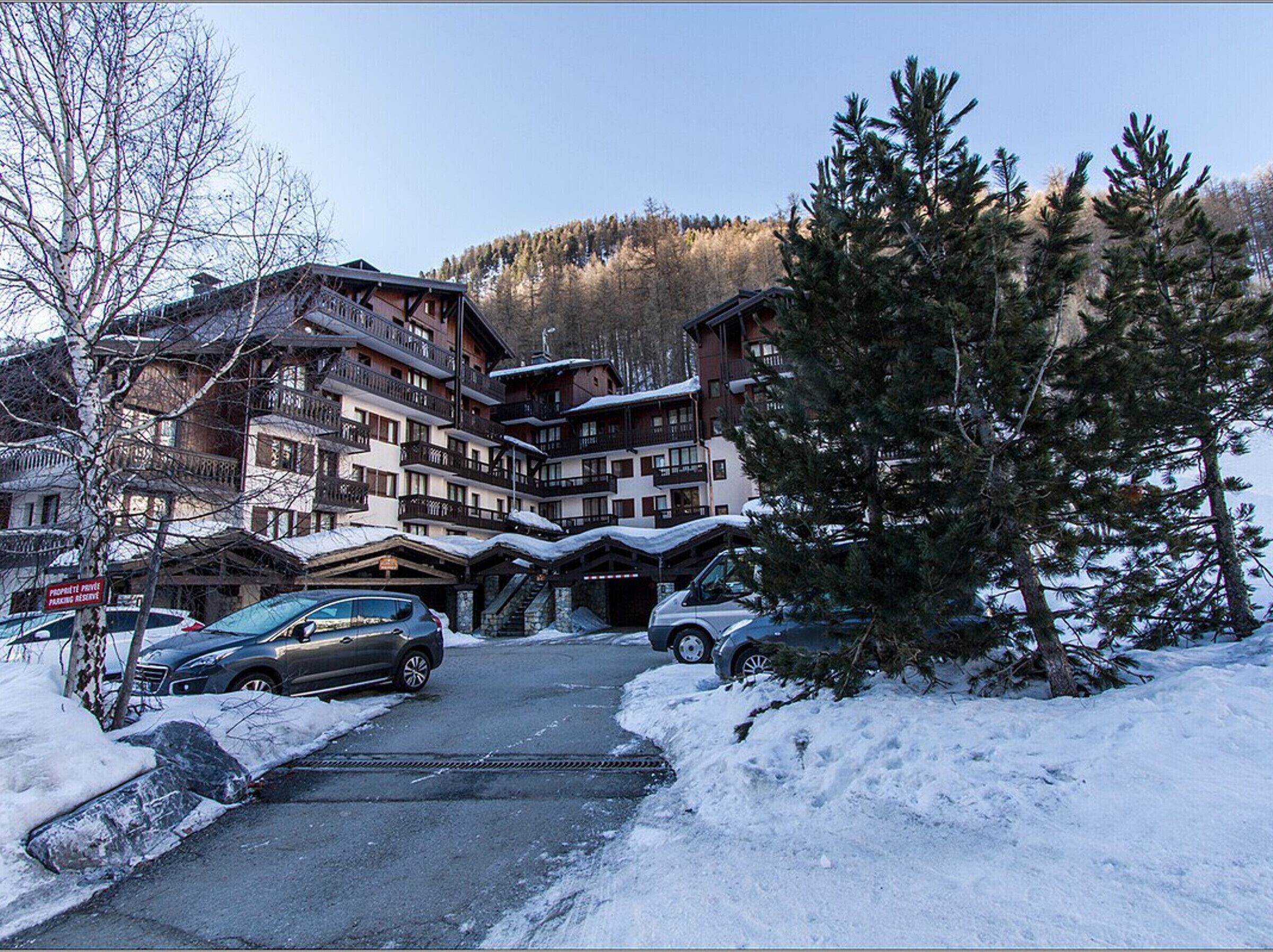 Un chalet à plusieurs étages, doté d'une entrée pour le télésiège, entouré d'arbres couverts de neige et surplombant un paysage montagneux.