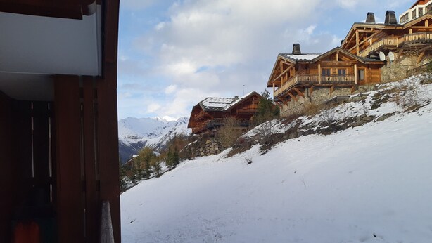 Eine Holzhütte mit Stein Fundament, vor einer Kulisse aus schneebedeckten Bergen und blauem Himmel.