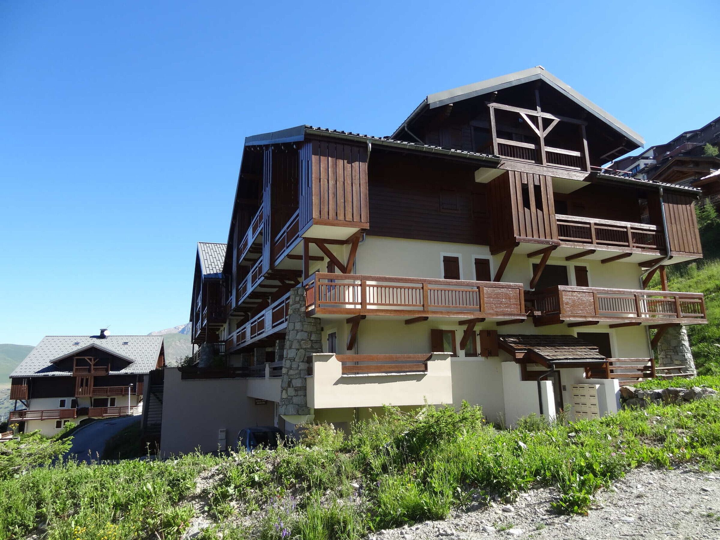 A multi-story chalet with wooden balconies and a stone foundation, surrounded by greenery.