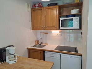A compact kitchen with wooden cabinets, a microwave, a coffee maker, and a dishwasher.