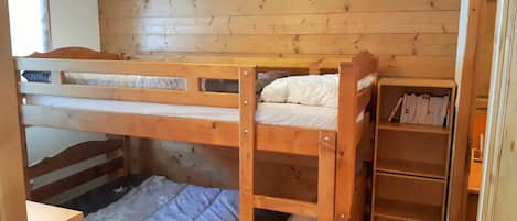 A bunk bed room with wooden walls and a bookshelf.