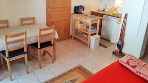 Eine kleine Küche mit Holzausstattung, einem Esstisch mit Stühlen, einer Kaffeemaschine und einem Staubsauger.