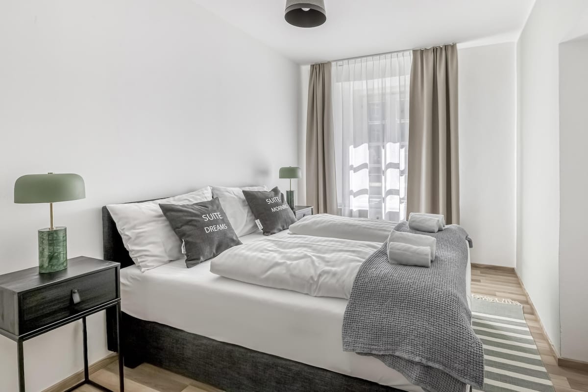A modern bedroom with a bed, bedside tables, and a window with curtains.