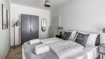 A modern bedroom with a large bed, a wardrobe, a mirror, and a floor lamp.