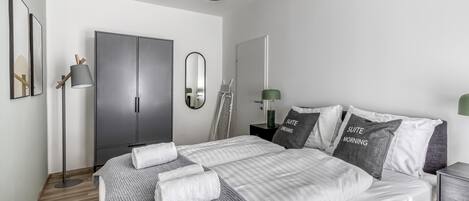 A modern bedroom with a large bed, a wardrobe, a mirror, and a floor lamp.